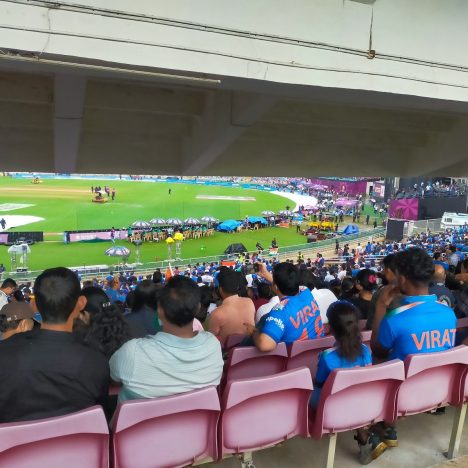 Spectators watch a cricket match from stadium seats.