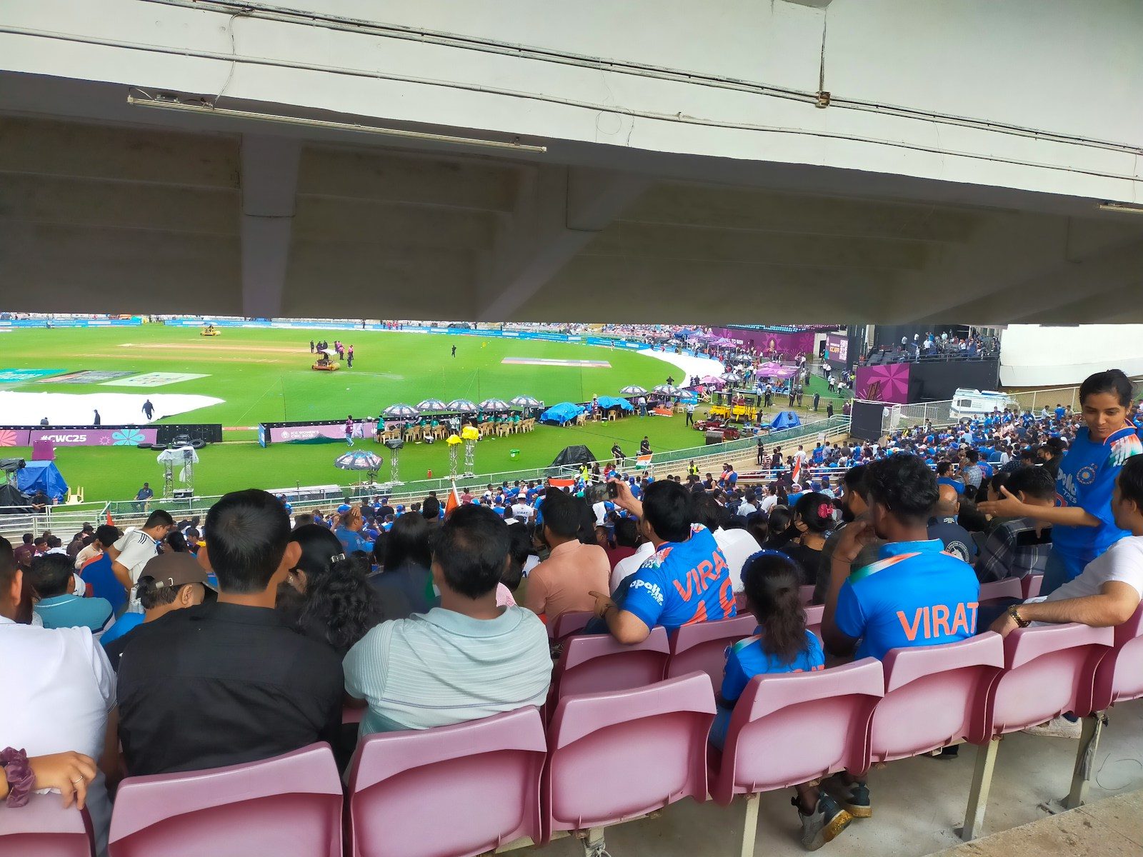 Spectators watch a cricket match from stadium seats.