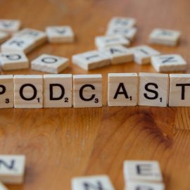 A wooden table topped with scrabble tiles that spell out the word podcast