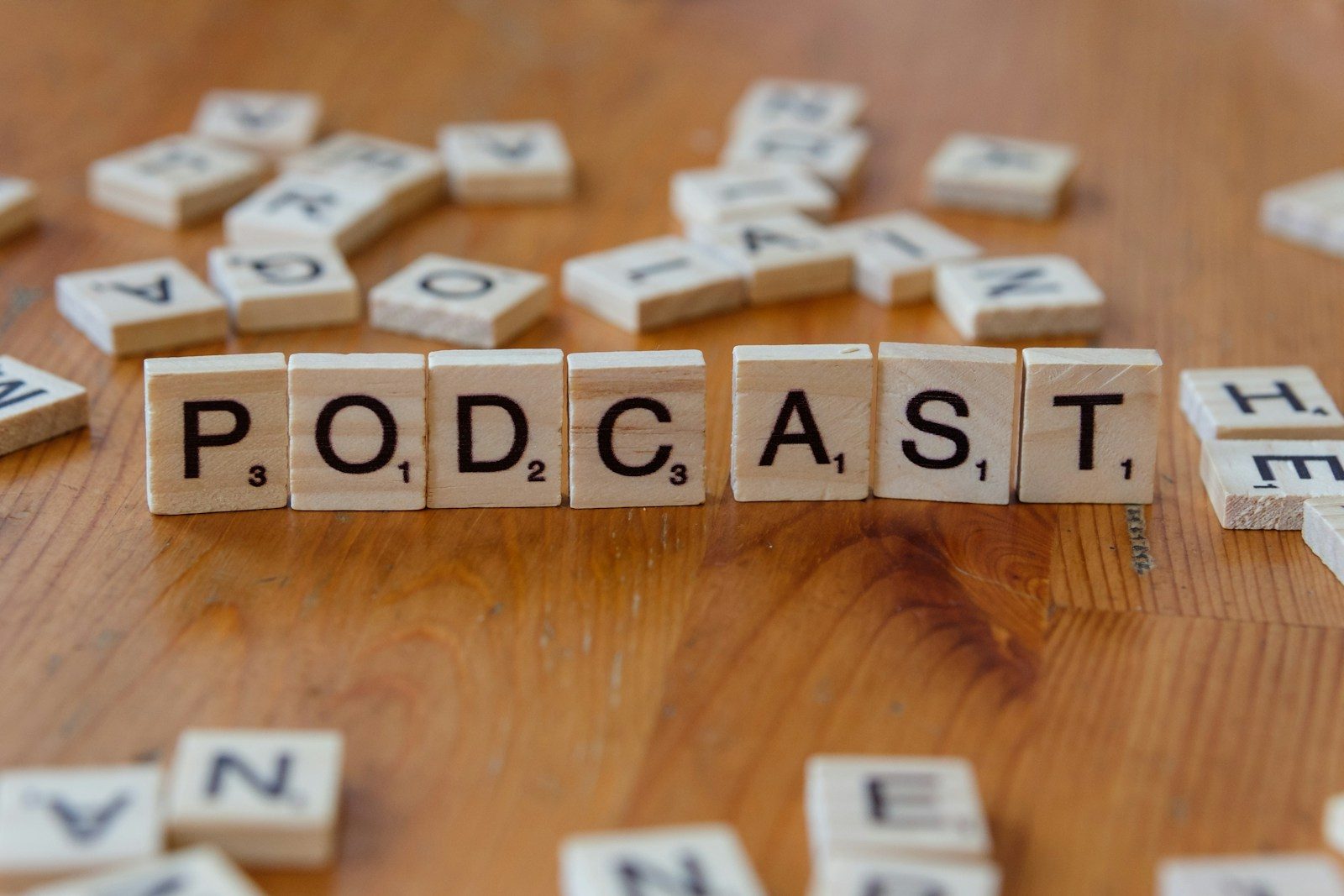 A wooden table topped with scrabble tiles that spell out the word podcast