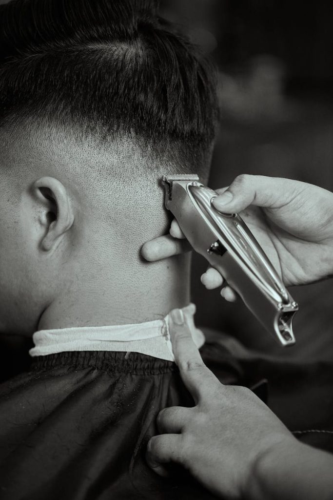 Detailed black and white close-up of a barber trimming a man's hair with clippers.