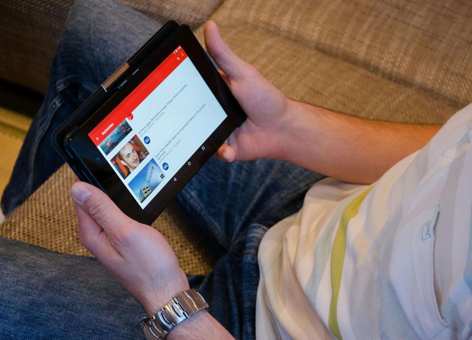 Close-up of a man holding a tablet while watching videos on a streaming app indoors.