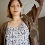 Caucasian woman holding a large question mark indoors, expressing curiosity.