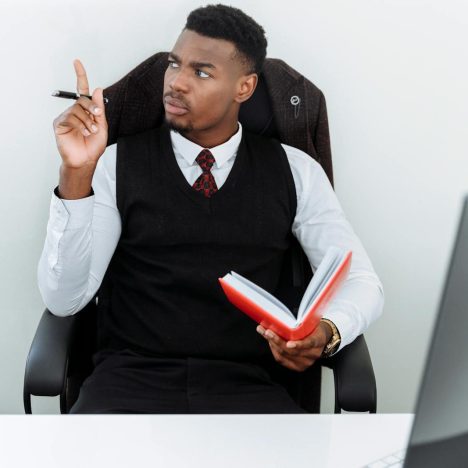 Young businessman thinking with a notebook and pen in a modern office setting, showing focus and intelligence.