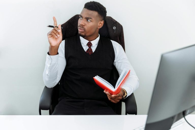 Young businessman thinking with a notebook and pen in a modern office setting, showing focus and intelligence.