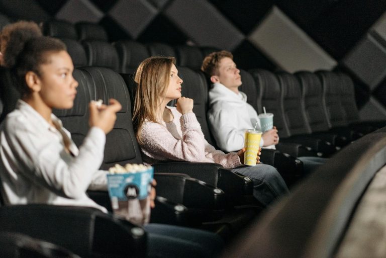 Three friends watching a movie while enjoying popcorn and drinks at a theater.