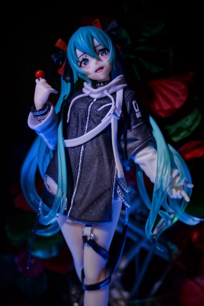 Anime figure with blue hair and black jacket holds candy.