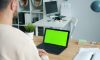 Man working on a laptop with a green screen.