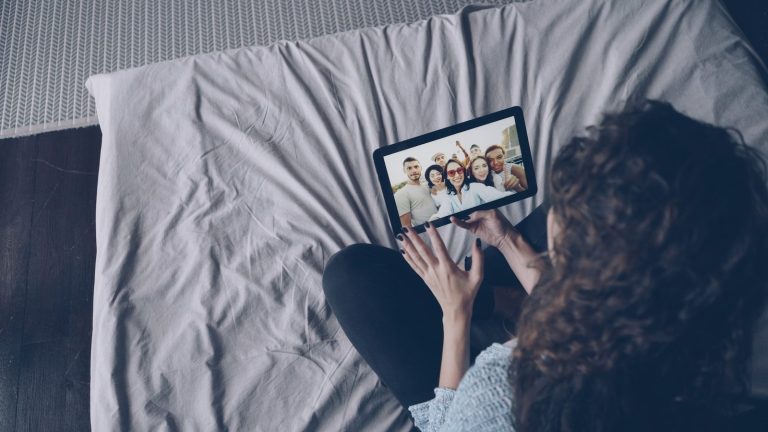 Woman video calling friends on tablet in bed