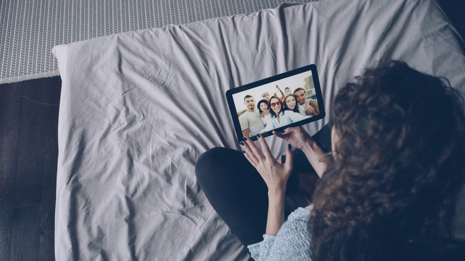 Woman video calling friends on tablet in bed