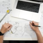 Designer sketching eyeglasses with laptop and tools.