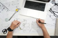 Designer sketching eyeglasses with laptop and tools.
