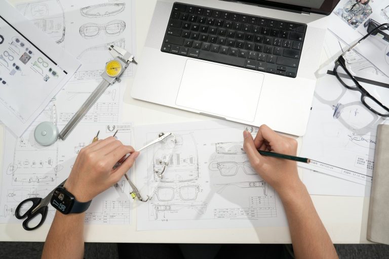 Designer sketching eyeglasses with laptop and tools.