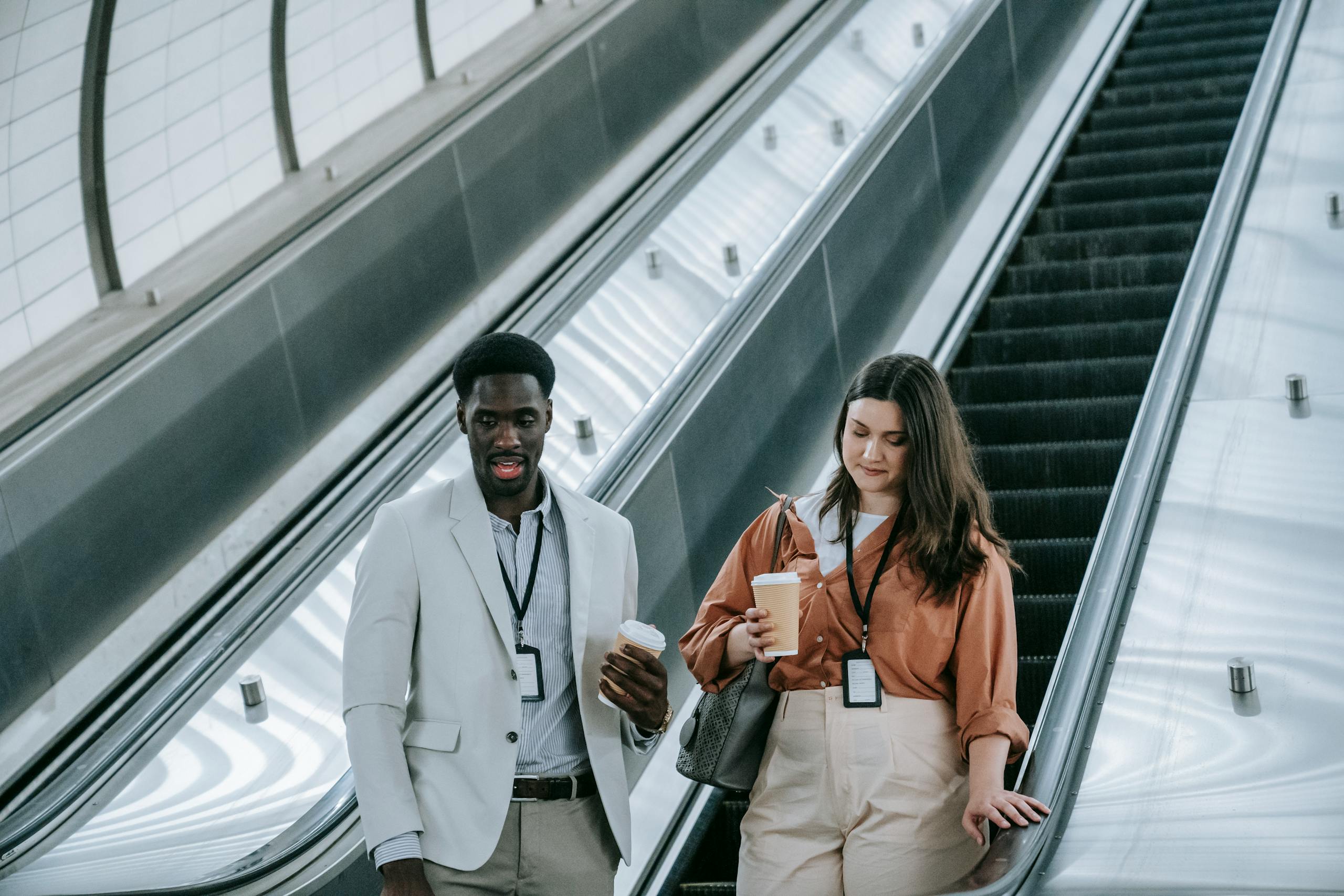 Two business professionals with ID badges use escalator in a contemporary office setting.