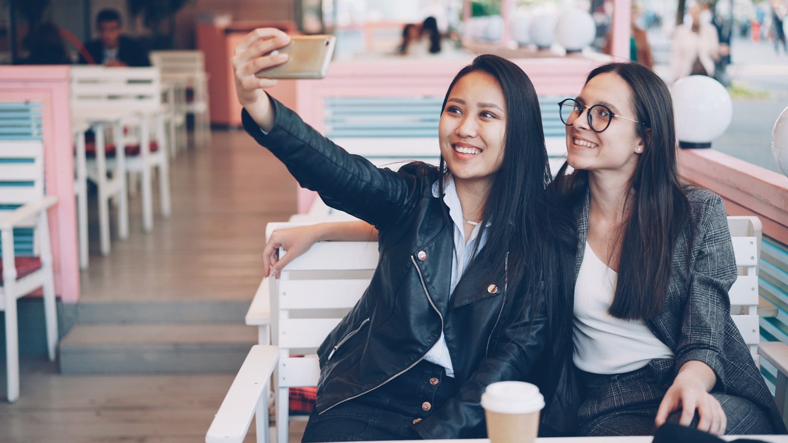 Two smiling friends taking a selfie at a cafe.