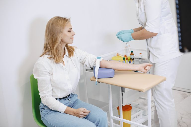 A woman sits in a clinic while a nurse prepares for a blood test procedure.
